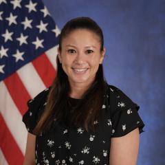 Woman smiling in front of American flag, wearing black floral top.