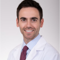 Man in white lab coat and maroon tie smiling at camera.