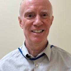 Portrait of a smiling bald man in a blue shirt.