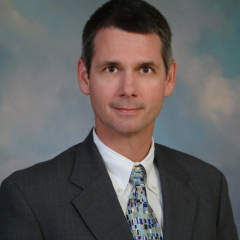 Professional headshot of a man in a gray suit and colorful tie.
