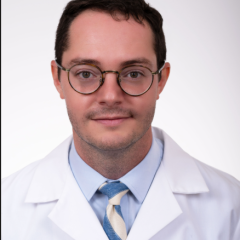 Smiling man in a white lab coat and blue tie with white stripes.