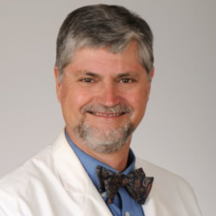 Smiling man in white lab coat and bowtie, headshot.