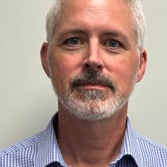 Man with white hair, beard, and mustache, wearing blue shirt.