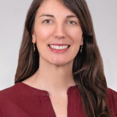 Portrait of a woman with long brown hair wearing a maroon shirt, smiling.