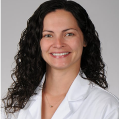 Woman with curly black hair and white lab coat smiling at camera.