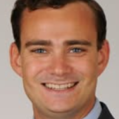 Headshot of a smiling man in a suit with blue shirt.