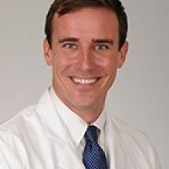 Portrait of a smiling man in a white lab coat and blue tie.
