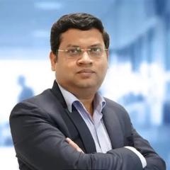Portrait of a man in a suit with arms crossed, blurred office background.