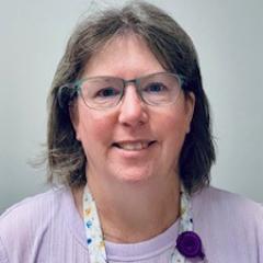 Woman with short hair wearing glasses and a purple shirt with a lanyard.