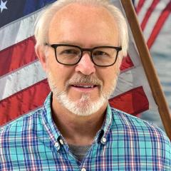 Headshot of a man with an American flag in the background.