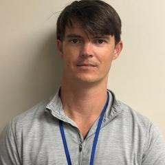 Headshot of a man in a gray polo shirt with a blue lanyard.