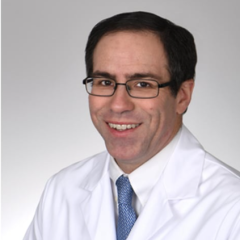 Smiling man in white lab coat and blue tie, wearing glasses.