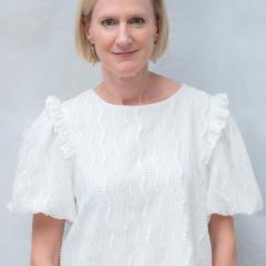 Portrait of a smiling woman with short blonde hair wearing a white blouse.