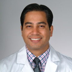 Man in a white lab coat and tie smiling for the camera.