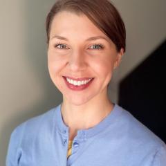 Portrait of a smiling woman in a blue shirt against a light background.