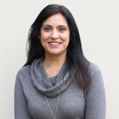 Woman with black hair wearing a gray sweater and scarf, smiling.