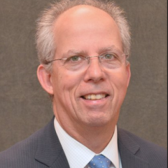 Man in a suit and blue tie smiling for the camera.