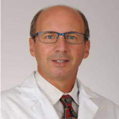 Man in white lab coat, blue tie, and glasses smiling for photo.