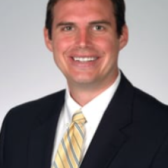 Man in black suit and yellow striped tie smiling.