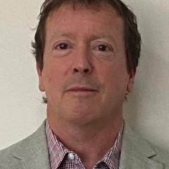 Headshot of a man in a gray blazer over a red and white checkered shirt.