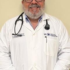 Male doctor in white coat with stethoscope around neck, smiling.