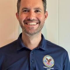 Man in blue polo shirt with logo smiling at camera.