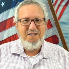 man smiling in front of flag