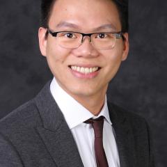 A smiling man in a gray suit and brown tie, wearing glasses.