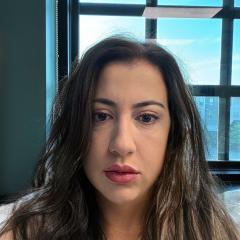 Woman with long dark hair and red lipstick, in front of a window.