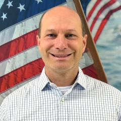 Portrait of smiling man in a white shirt against American flag background.
