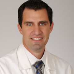 Smiling man in white lab coat and striped tie.