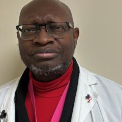 A bald man in a red turtleneck and white coat, looking at the camera.