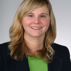 Portrait of a smiling woman with blonde hair wearing a green shirt and black blazer.