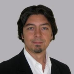 A man with black hair and a beard wearing a white shirt and black jacket.