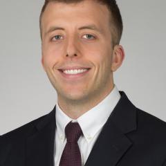 Man in black suit and maroon tie smiling at camera.