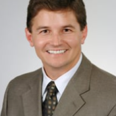 Headshot of a man in a suit and tie smiling.