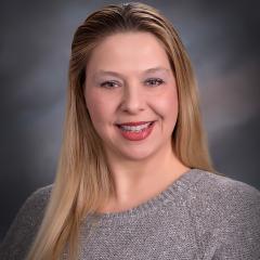 Portrait of a woman with long blonde hair, smiling in a gray sweater.