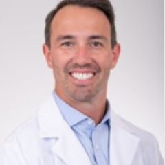 Portrait of a man in a white lab coat smiling.