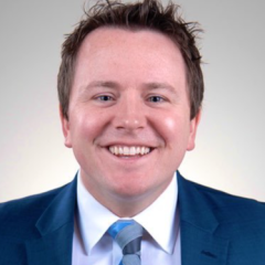 Headshot of a man in a blue suit and tie smiling.