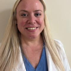 Photo of a smiling woman with blonde hair wearing a white lab coat and blue shirt.
