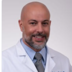 Smiling bald man in white lab coat and gray tie.