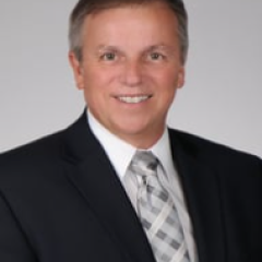 Man in black suit and checkered tie smiling at the camera.