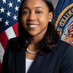 Smiling woman in business suit with American flag and US Army flag in background.