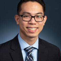 Portrait of a man wearing glasses, suit, and striped tie smiling at the camera.