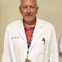 Smiling man in white lab coat with stethoscope around his neck.