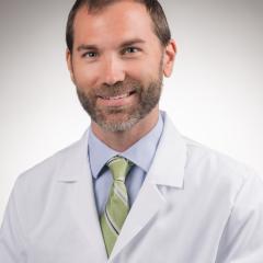 Man in white lab coat and green tie smiling for the camera.