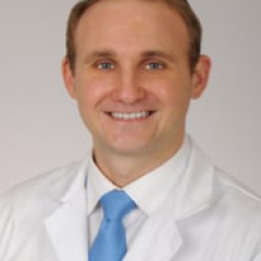 Smiling man in white lab coat and blue tie, headshot.