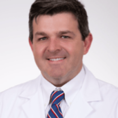 Smiling man in white lab coat and red, white, and blue tie.