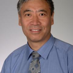 A smiling Asian man in a blue shirt and gray tie.