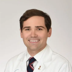 Smiling man in white lab coat and striped tie.